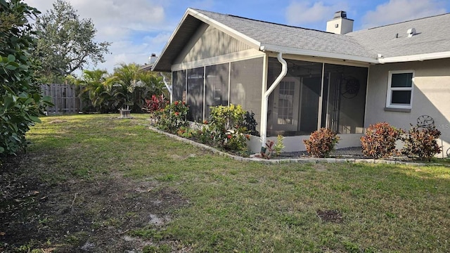 view of side of home with a lawn, a sunroom, a chimney, roof with shingles, and fence