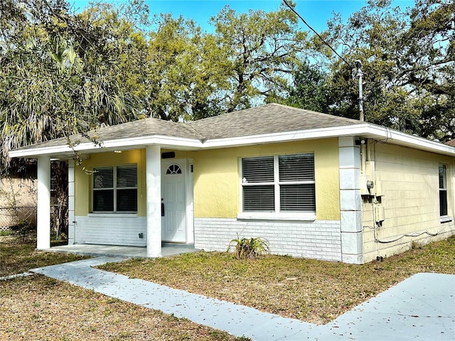 view of front facade featuring roof with shingles, a porch, and brick siding