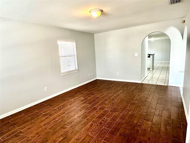 spare room featuring arched walkways, baseboards, and wood finished floors