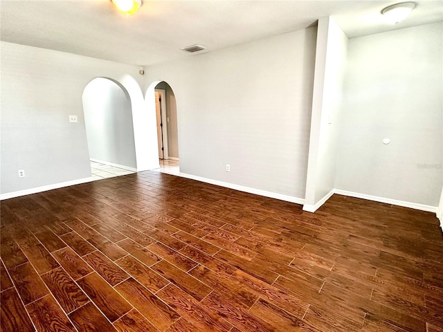 spare room featuring arched walkways, visible vents, baseboards, and wood finished floors