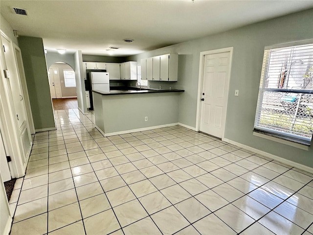 kitchen with arched walkways, light tile patterned floors, a peninsula, visible vents, and dark countertops