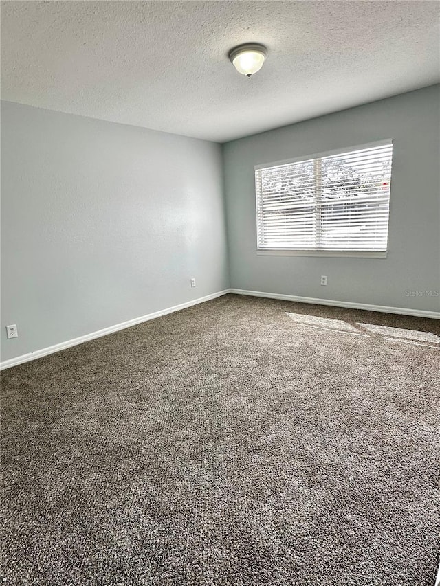 carpeted spare room featuring a textured ceiling and baseboards