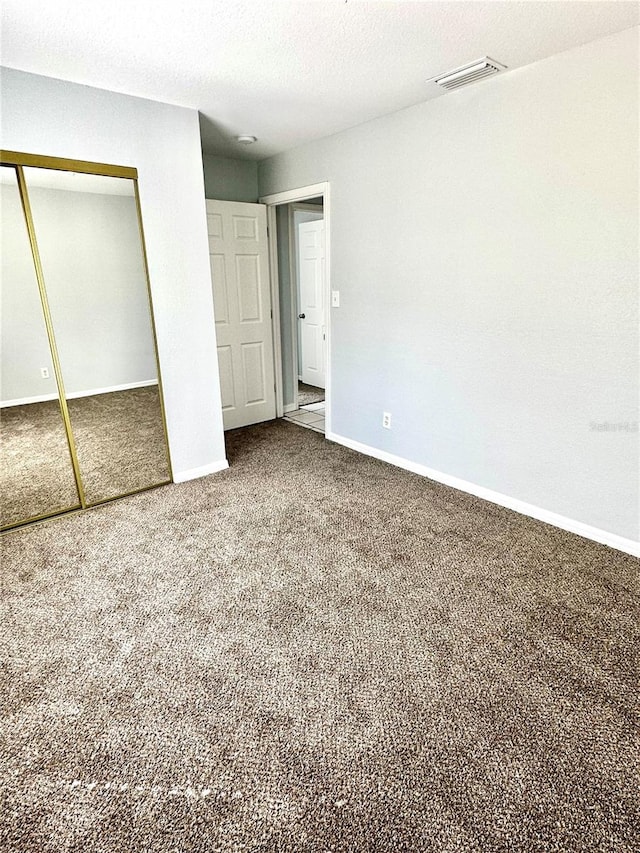 unfurnished bedroom with a textured ceiling, carpet floors, visible vents, baseboards, and a closet