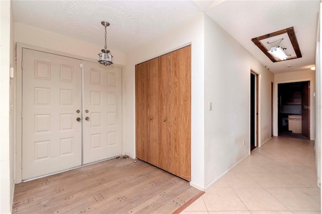 foyer entrance featuring light tile patterned flooring, a textured ceiling, and baseboards