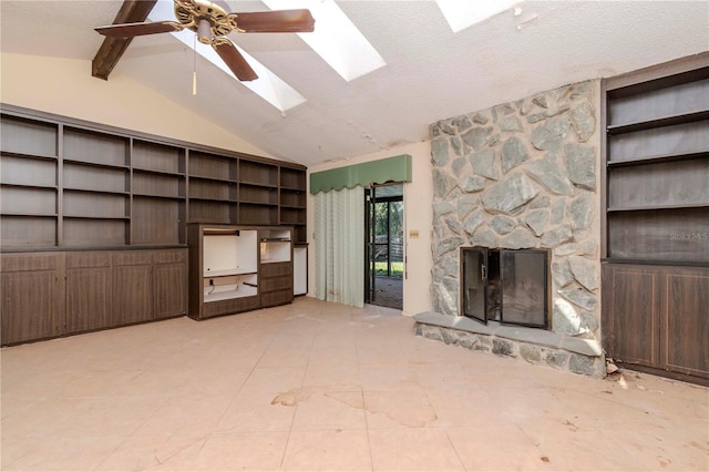 unfurnished living room featuring a textured ceiling, a stone fireplace, a ceiling fan, tile patterned floors, and lofted ceiling with skylight