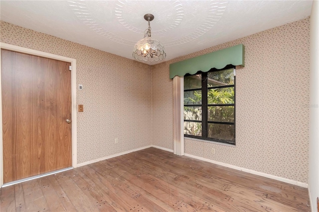 unfurnished room featuring a notable chandelier, hardwood / wood-style floors, a textured ceiling, baseboards, and wallpapered walls