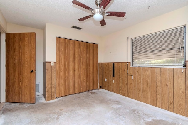 unfurnished bedroom with a textured ceiling, wood walls, a closet, and visible vents