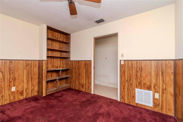 carpeted spare room featuring wainscoting, visible vents, and wooden walls