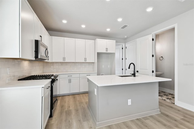 4717 W Mccoy St Unit 9, Tampa, FL 33616 - kitchen featuring a sink, stainless steel microwave, gas range, an island with sink, and light wood-style floors