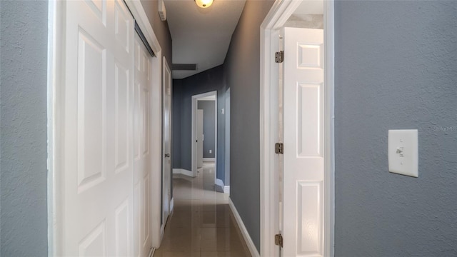 hall featuring tile patterned flooring, visible vents, baseboards, and a textured wall