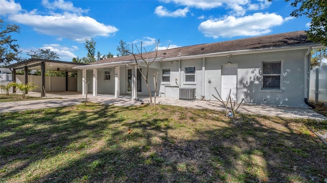 rear view of property featuring central AC unit, a lawn, an attached carport, fence, and stucco siding