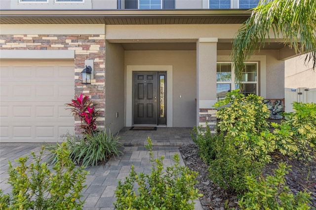 entrance to property with a garage, stone siding, and stucco siding