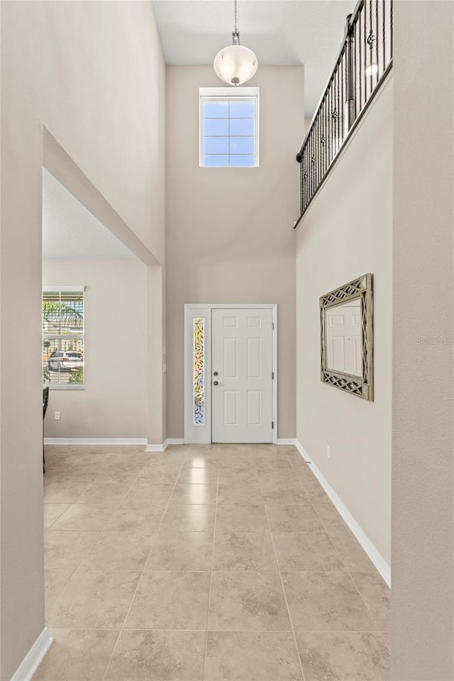 foyer with tile patterned floors, a towering ceiling, and baseboards