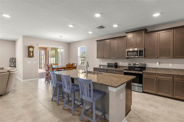 kitchen with a sink, visible vents, appliances with stainless steel finishes, dark stone counters, and a center island with sink