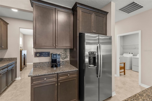 kitchen featuring stainless steel fridge, visible vents, dark stone countertops, washing machine and clothes dryer, and dark brown cabinets