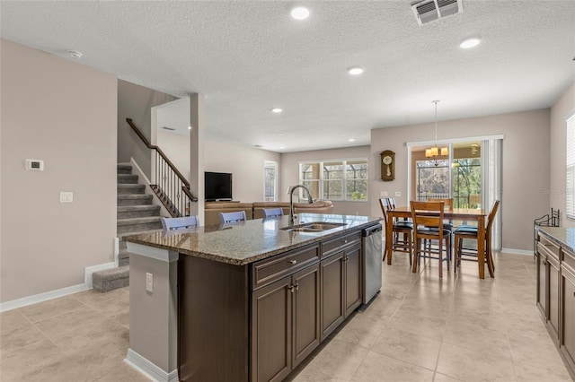 kitchen with visible vents, dark stone counters, dishwasher, dark brown cabinets, and a sink