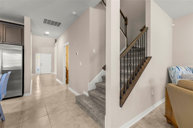 staircase featuring tile patterned flooring, visible vents, a textured ceiling, and baseboards