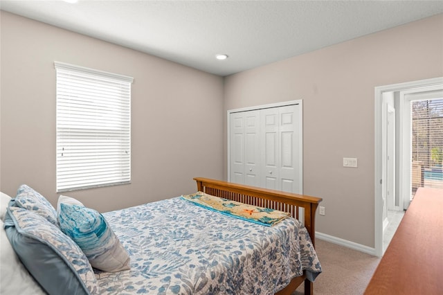 bedroom with a closet, light carpet, a textured ceiling, and baseboards