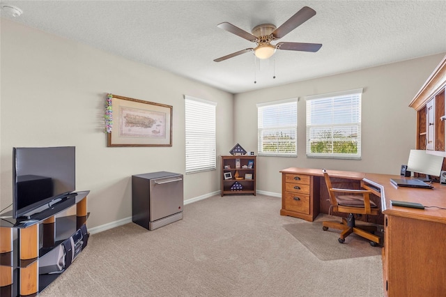 home office featuring a textured ceiling, ceiling fan, baseboards, and light colored carpet