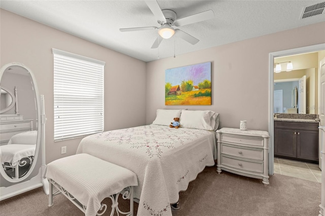 bedroom with light carpet, visible vents, a ceiling fan, ensuite bathroom, and a textured ceiling