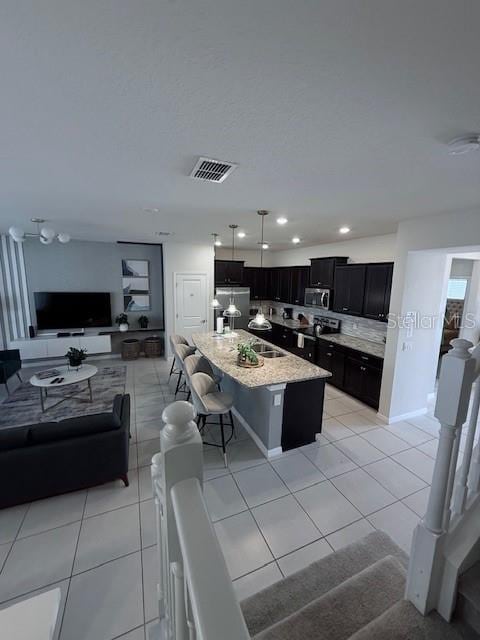 kitchen with light tile patterned floors, dark cabinetry, stainless steel microwave, and a breakfast bar