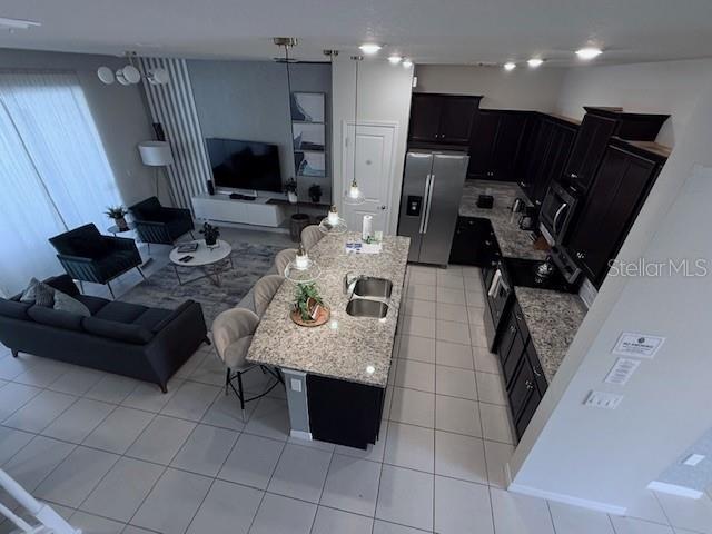 kitchen featuring light stone counters, light tile patterned floors, open floor plan, dark cabinets, and stainless steel fridge