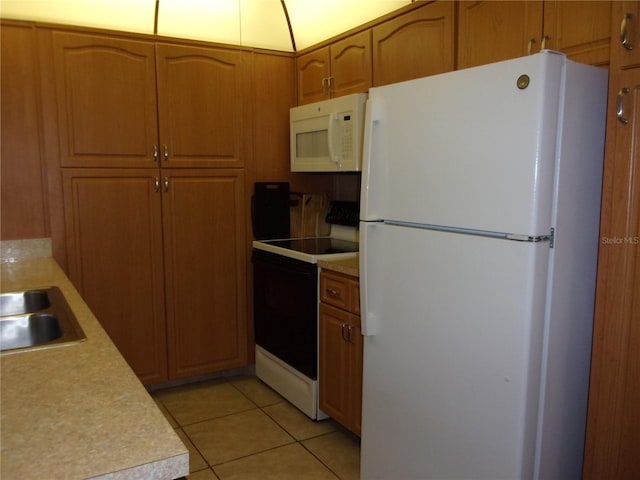 kitchen with white appliances, brown cabinetry, light countertops, a sink, and light tile patterned flooring