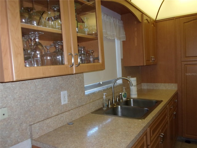 kitchen with tasteful backsplash, a sink, glass insert cabinets, and brown cabinets