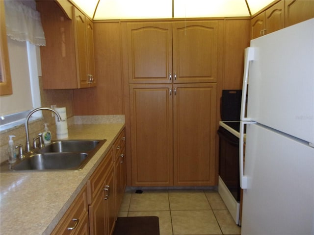 kitchen featuring light tile patterned floors, range with electric cooktop, a sink, freestanding refrigerator, and brown cabinets