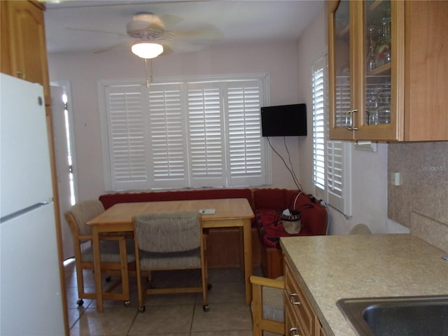 kitchen featuring light tile patterned floors, ceiling fan, light countertops, freestanding refrigerator, and glass insert cabinets