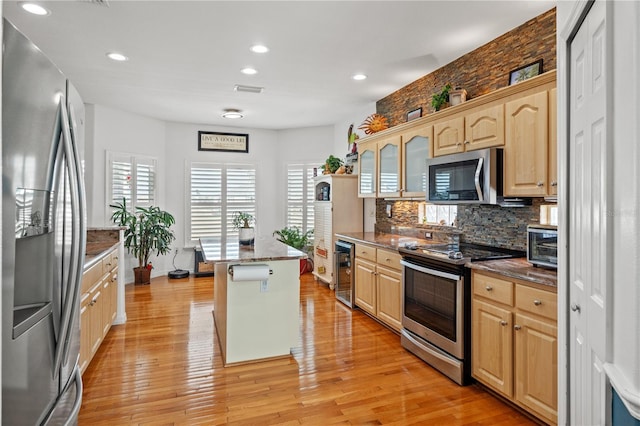 kitchen with wine cooler, backsplash, appliances with stainless steel finishes, light brown cabinets, and light wood-type flooring