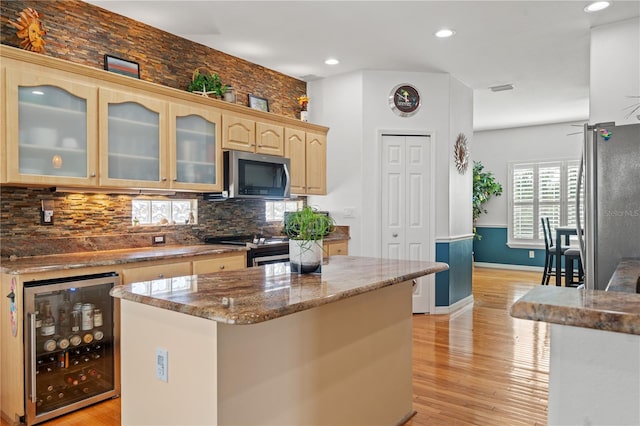 kitchen with beverage cooler, light wood-style flooring, a kitchen island, stainless steel appliances, and light brown cabinets