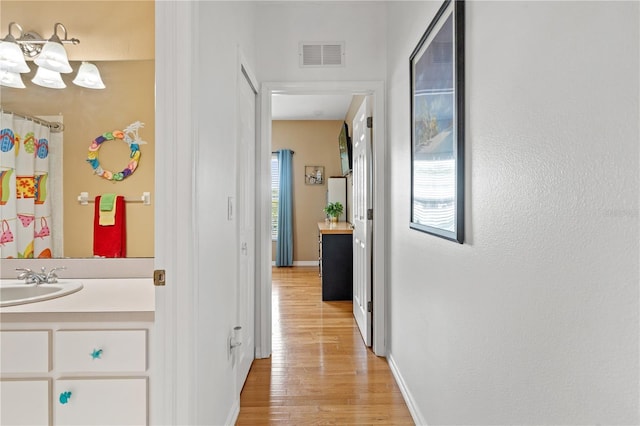 hall featuring visible vents, a sink, light wood-style flooring, and baseboards