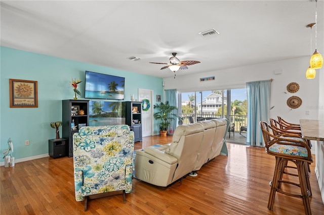 living area featuring hardwood / wood-style flooring, ceiling fan, visible vents, and baseboards