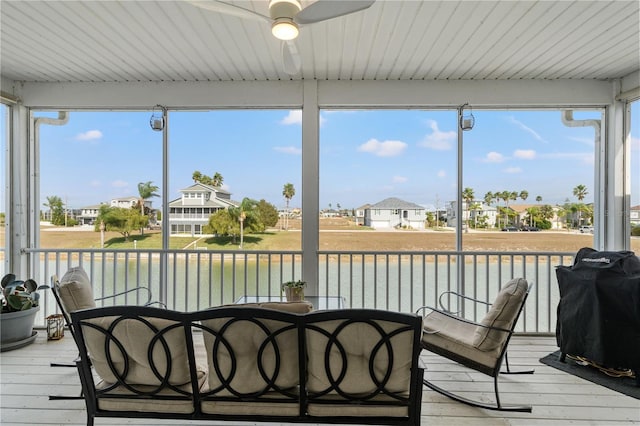 sunroom with a water view, a healthy amount of sunlight, a residential view, and a ceiling fan