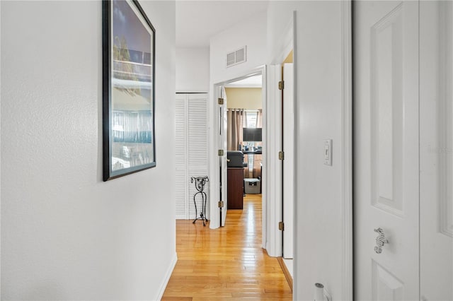 hallway featuring light wood finished floors, visible vents, and baseboards