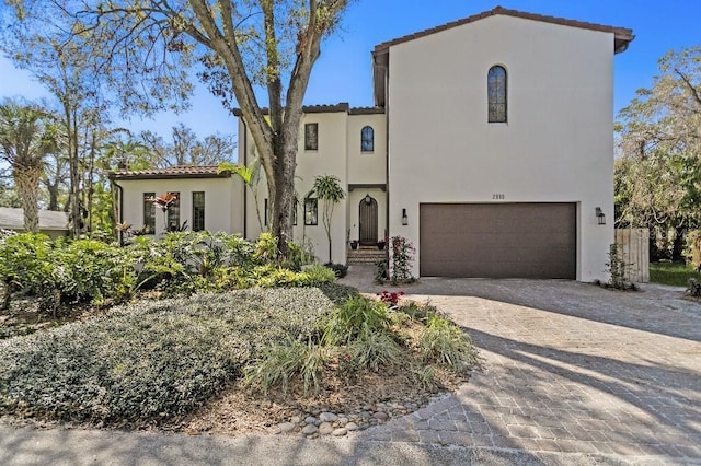 mediterranean / spanish house featuring an attached garage, a tile roof, decorative driveway, and stucco siding