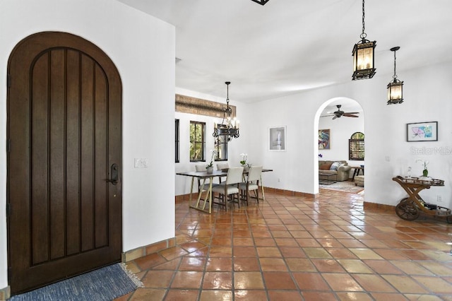 tiled entryway featuring arched walkways, ceiling fan with notable chandelier, and baseboards