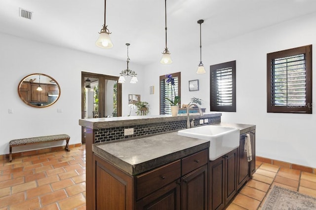 kitchen featuring a center island with sink, visible vents, dark countertops, decorative light fixtures, and a sink