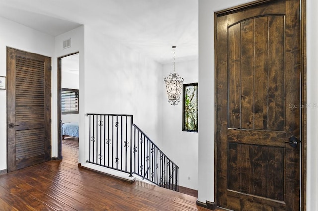 hallway with visible vents, baseboards, an upstairs landing, hardwood / wood-style floors, and an inviting chandelier