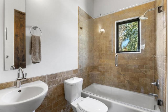 full bathroom featuring toilet, enclosed tub / shower combo, tile walls, and a sink