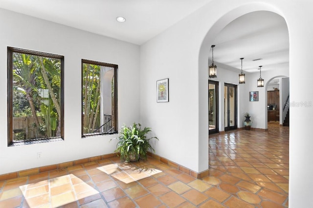 corridor featuring arched walkways, tile patterned flooring, recessed lighting, visible vents, and baseboards