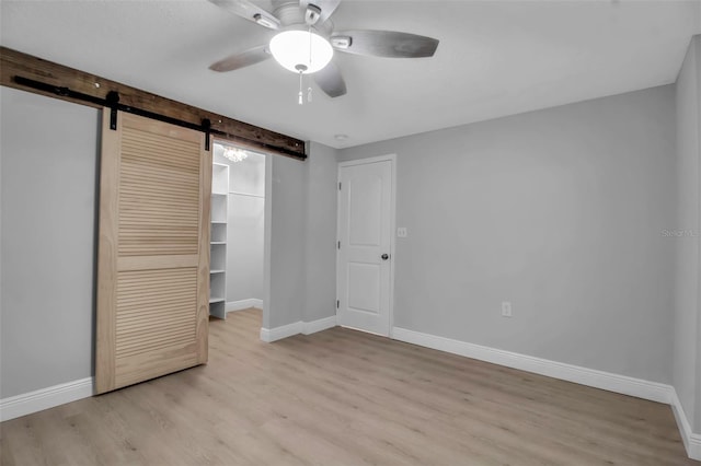 7 Georgia Ave, Crystal Beach, FL 34681 - unfurnished bedroom featuring a walk in closet, baseboards, light wood-style floors, and a barn door