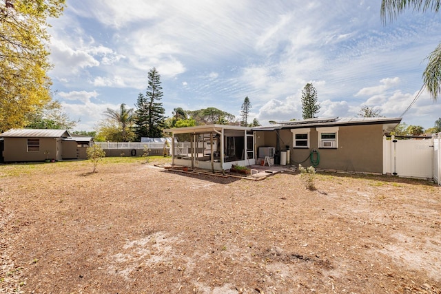 rear view of house with an outbuilding, a fenced backyard, a sunroom, a gate, and stucco siding