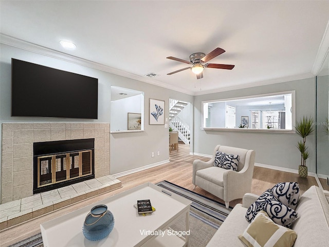 living area with crown molding, visible vents, a tiled fireplace, wood finished floors, and baseboards