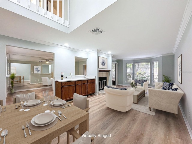 dining room with light wood finished floors, visible vents, a tiled fireplace, ornamental molding, and baseboards