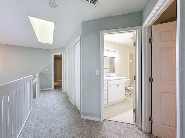 hall with light carpet, visible vents, and baseboards