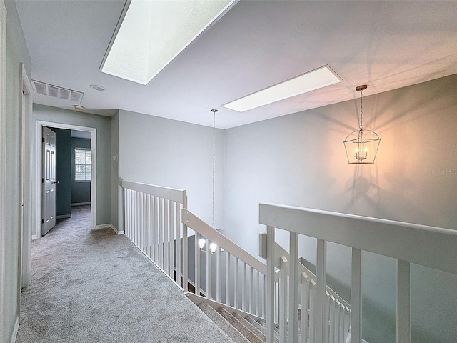 hall with a skylight, carpet flooring, visible vents, an upstairs landing, and an inviting chandelier