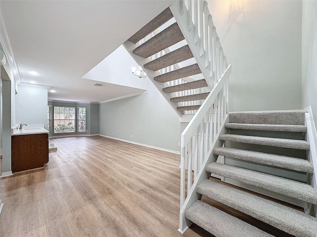 stairs with visible vents, baseboards, crown molding, and wood finished floors