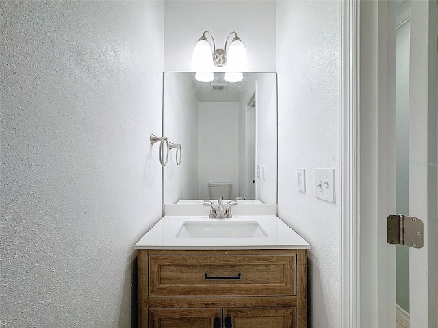 half bath featuring toilet, a textured wall, visible vents, and vanity